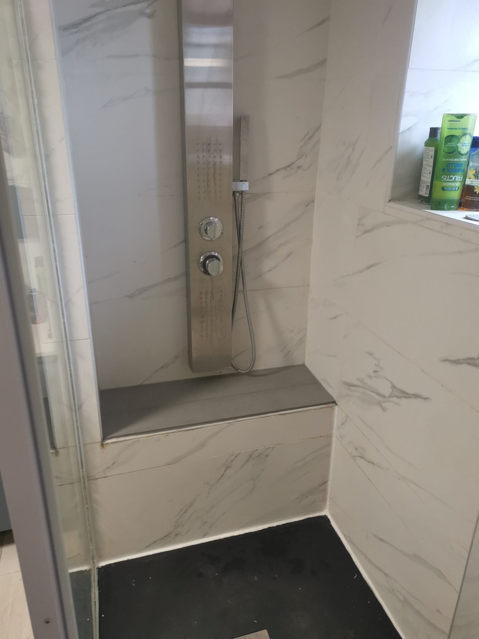 Détail d'une douche italienne avec carrelage mural effet marbre, niches de rangement et robinetterie encastrée.